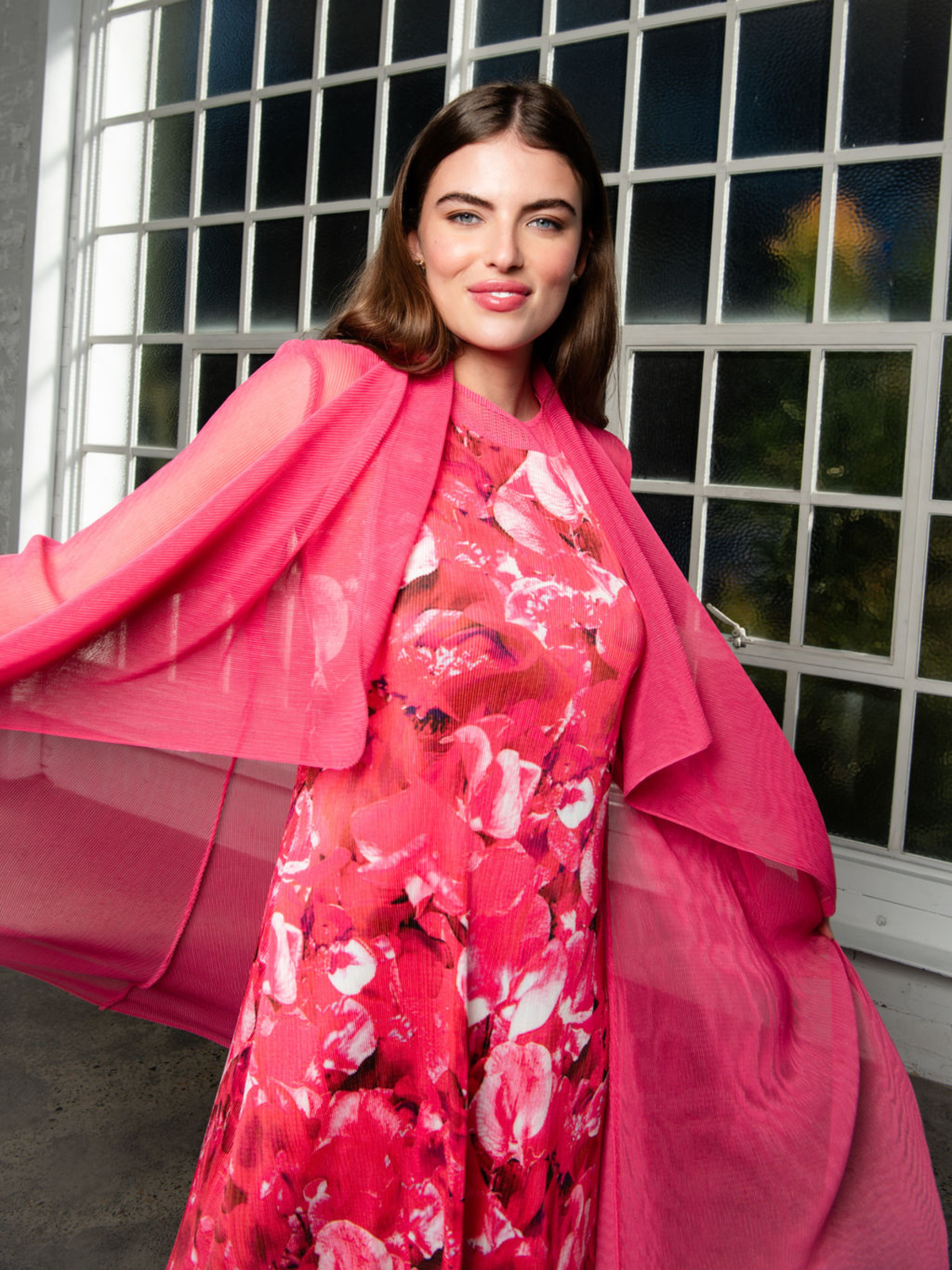 Woman wearing a pink floral dress with a matching pink shawl in front of a window.